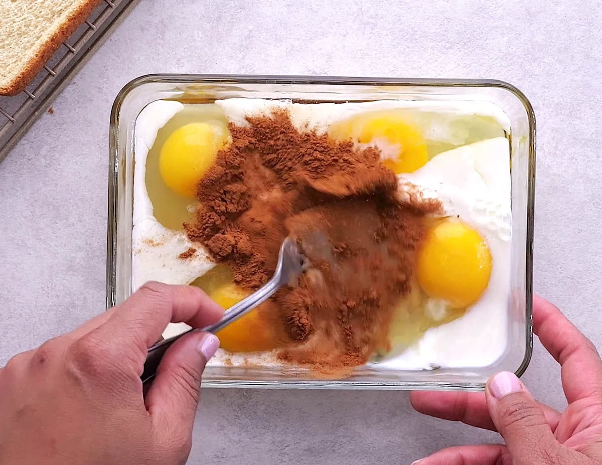 Hand whisking eggs, milk, and ground cinnamon together.