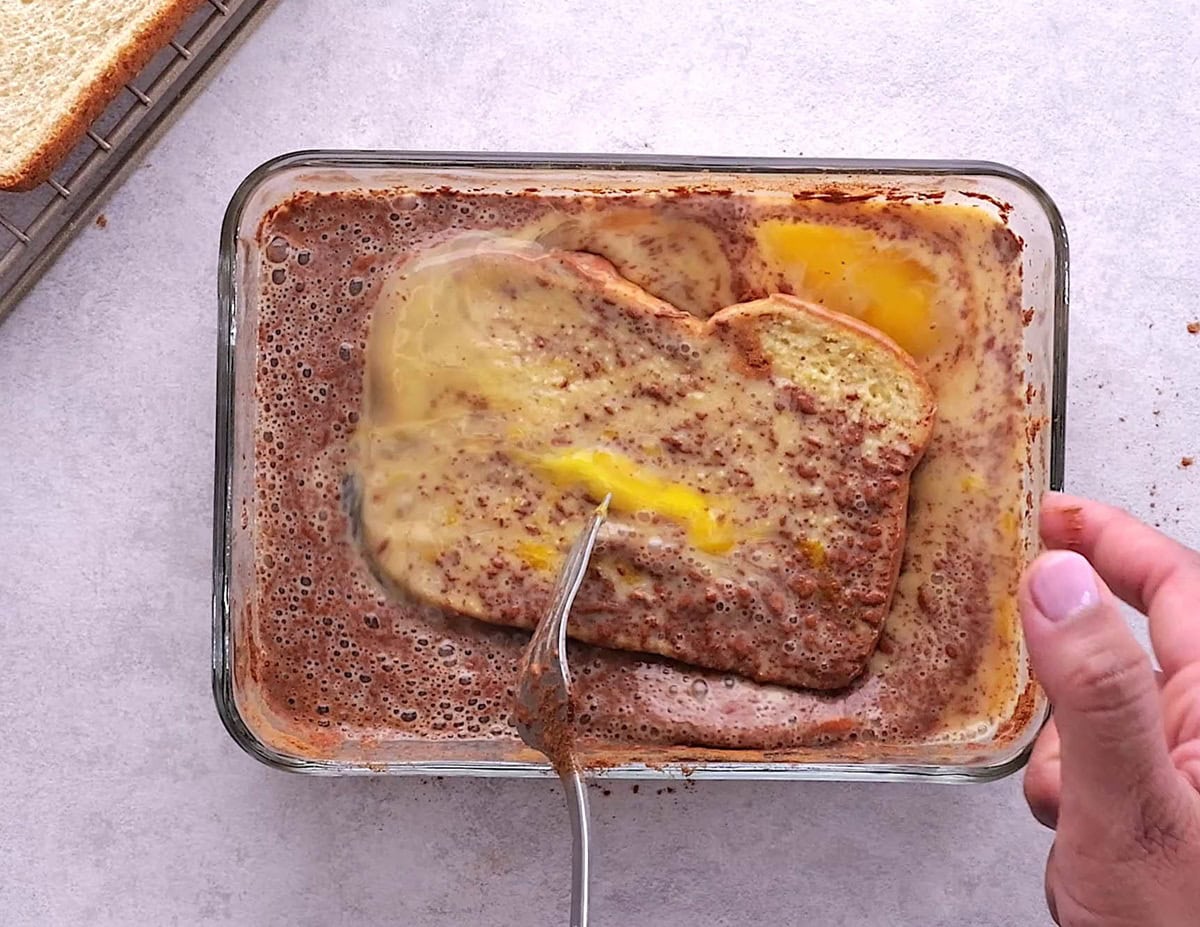 Shallow dish of toast soaking in egg and milk to make breakfast.