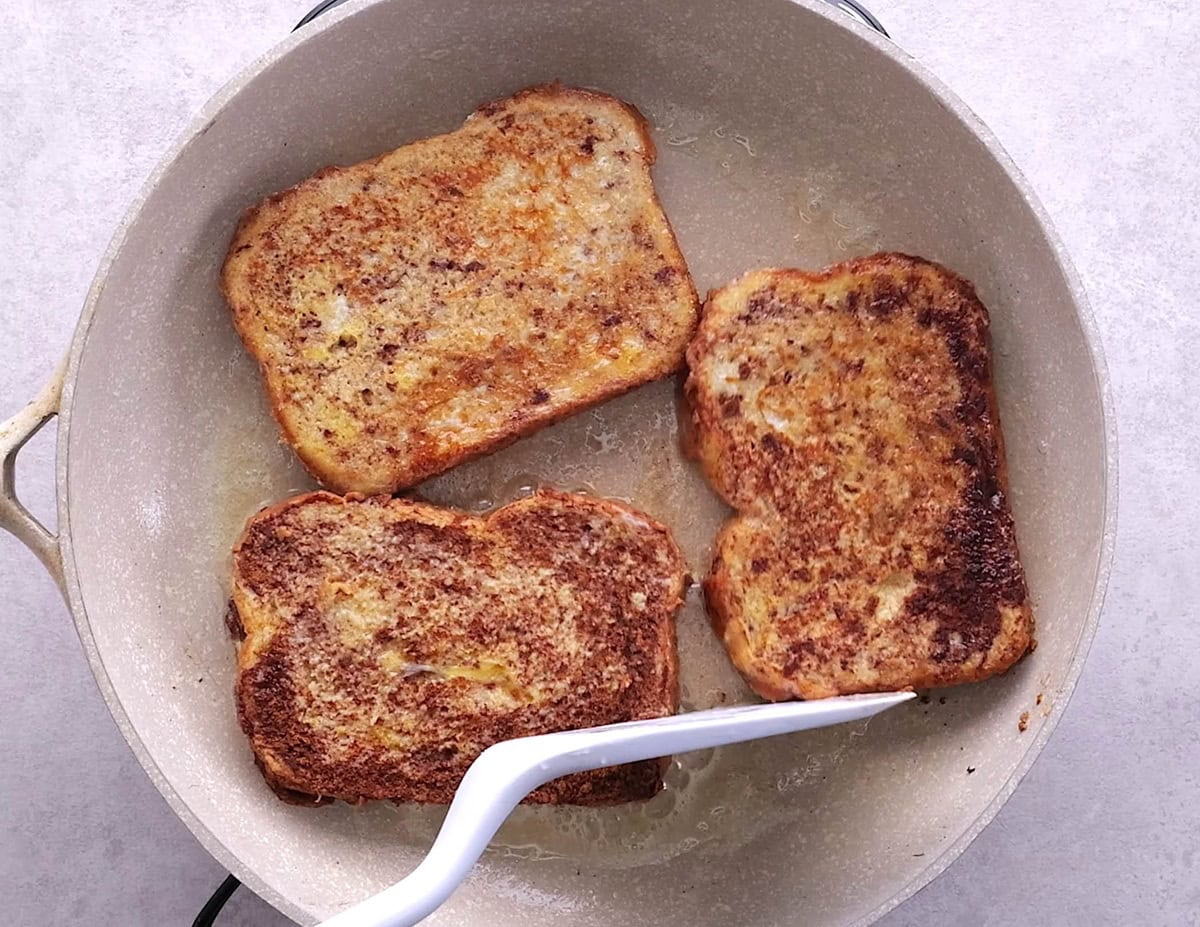 Three slices of toast cooking in a frying pan.