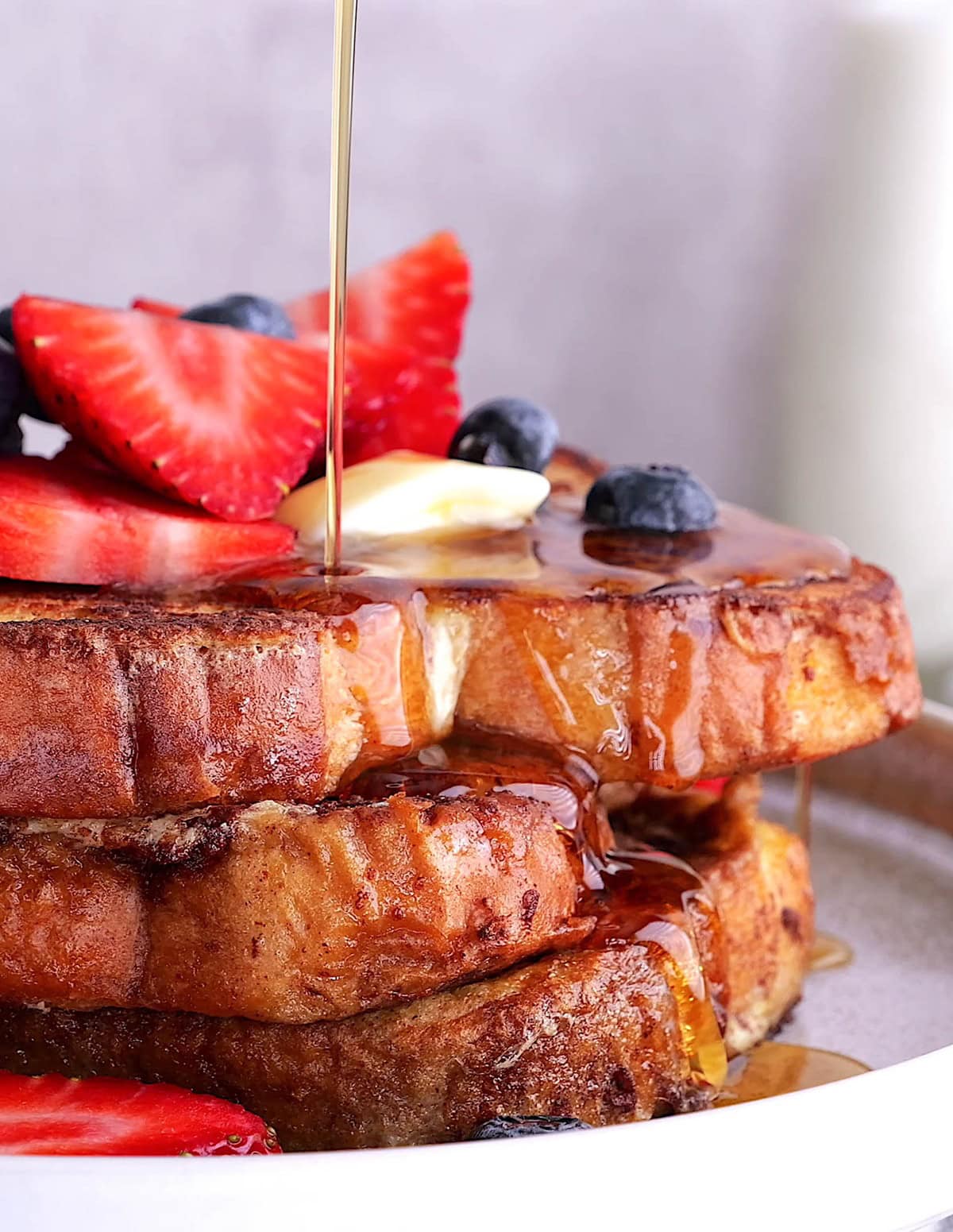 Stack of French toast with butter and berries on top, be drizzled with pure maple syrup.