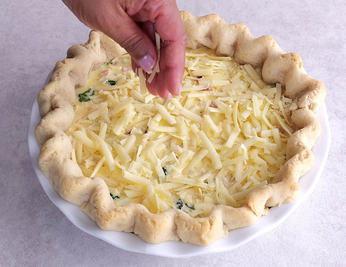 Hand sprinkling grated cheese over the quiche.