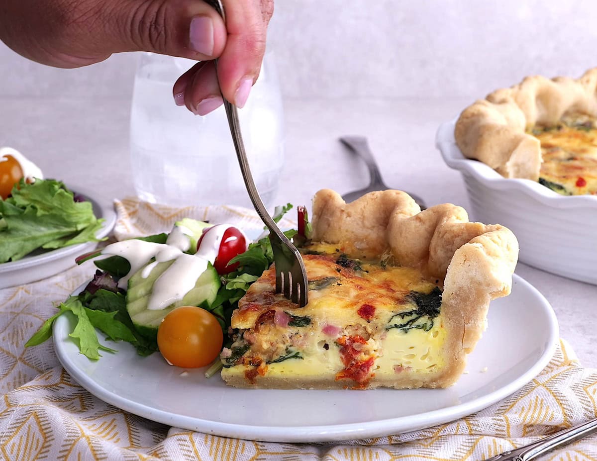 Hand taking a bite out of a slice of quiche.