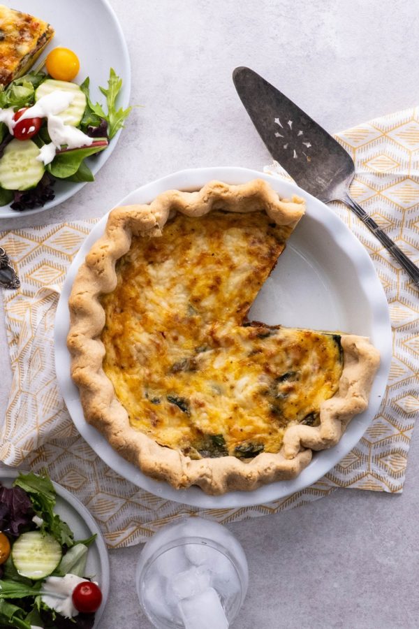 Quiche on a table with a slice taken out and a plate of salad.