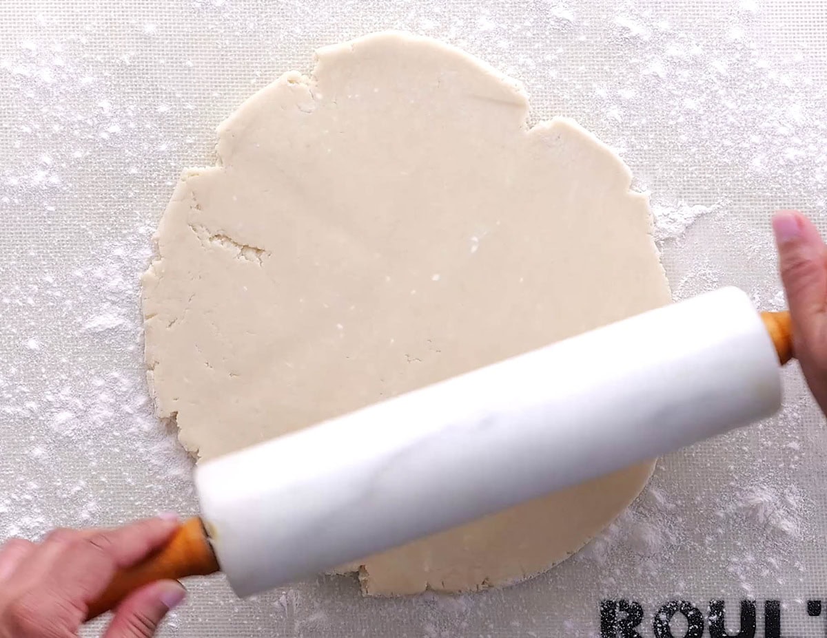 Person holding a rolling pin, rolling out pie crust dough.