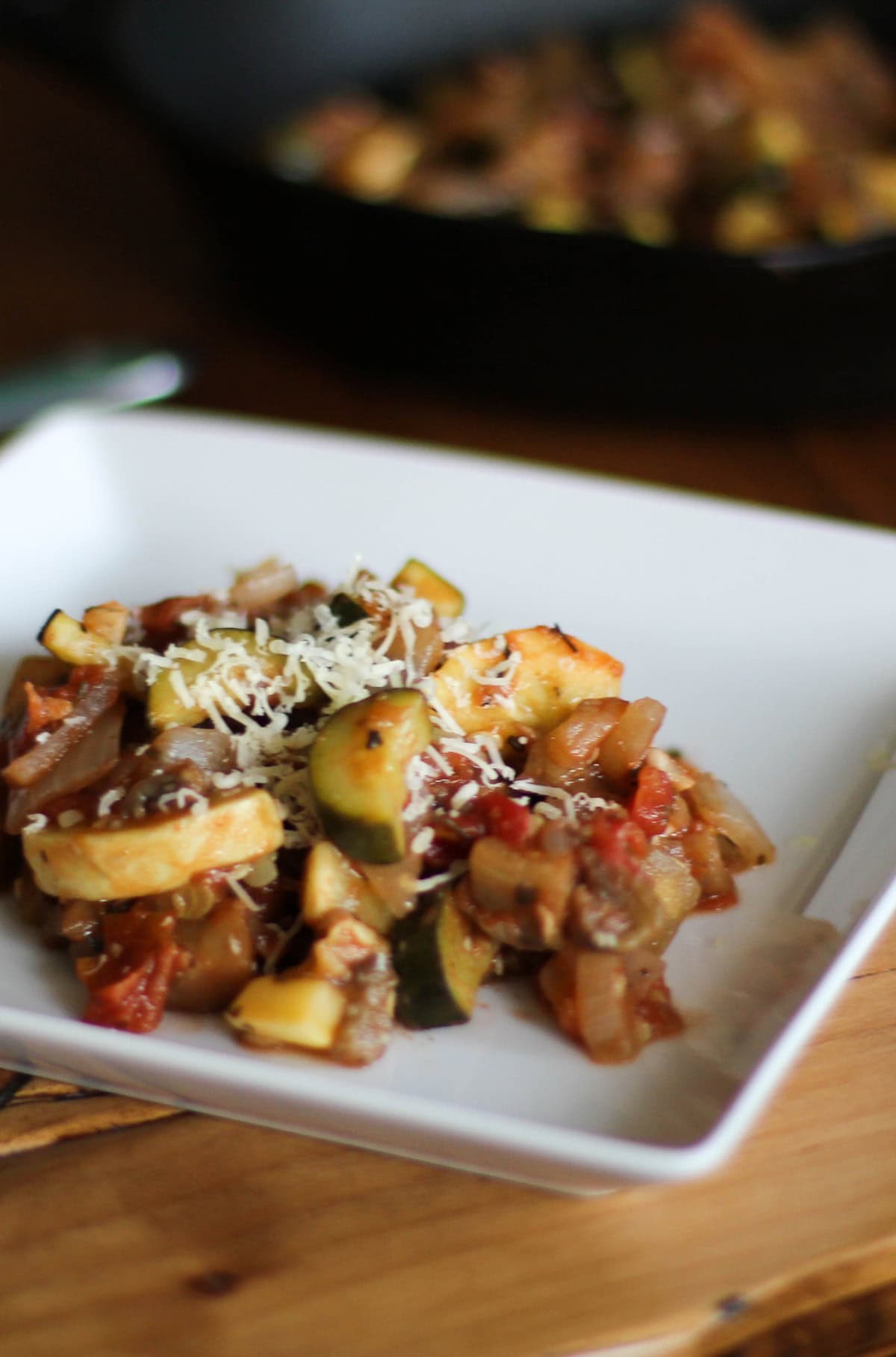 Ratatouille on a white plate with the rest of the skillet of eggplant and zucchini in the background.