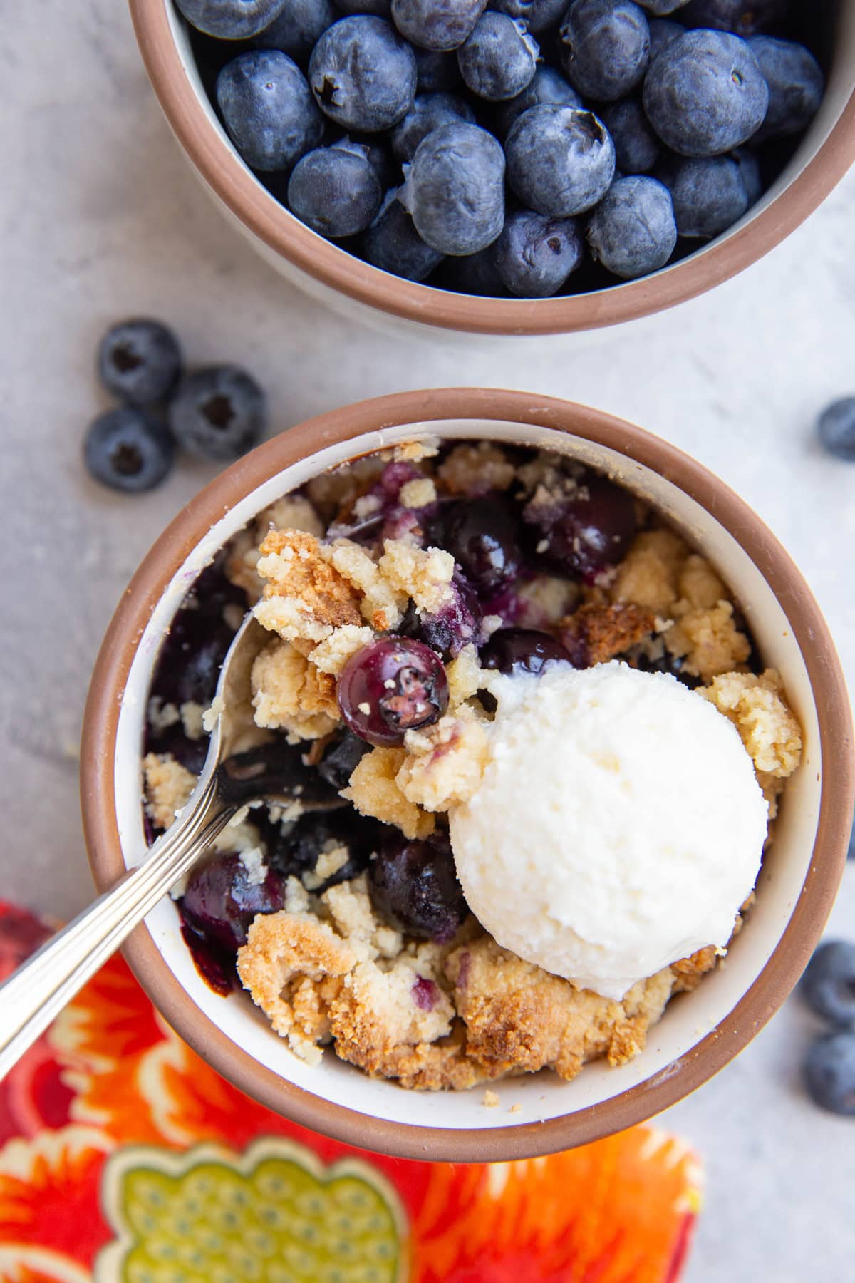 Ramekin full of berry crisp with a spoon taking a scoop and a little ice cream to the side.