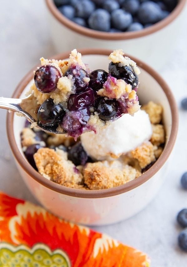 Ramekin of blueberry crisp with a spoon full of crisp ready to take a bite.