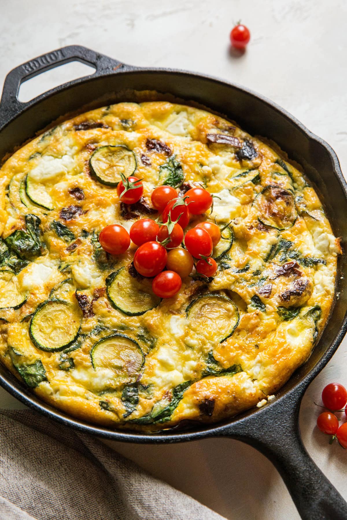 Cast iron skillet with zucchini frittata with cherry tomatoes on top. Ready to serve for breakfast or brunch.