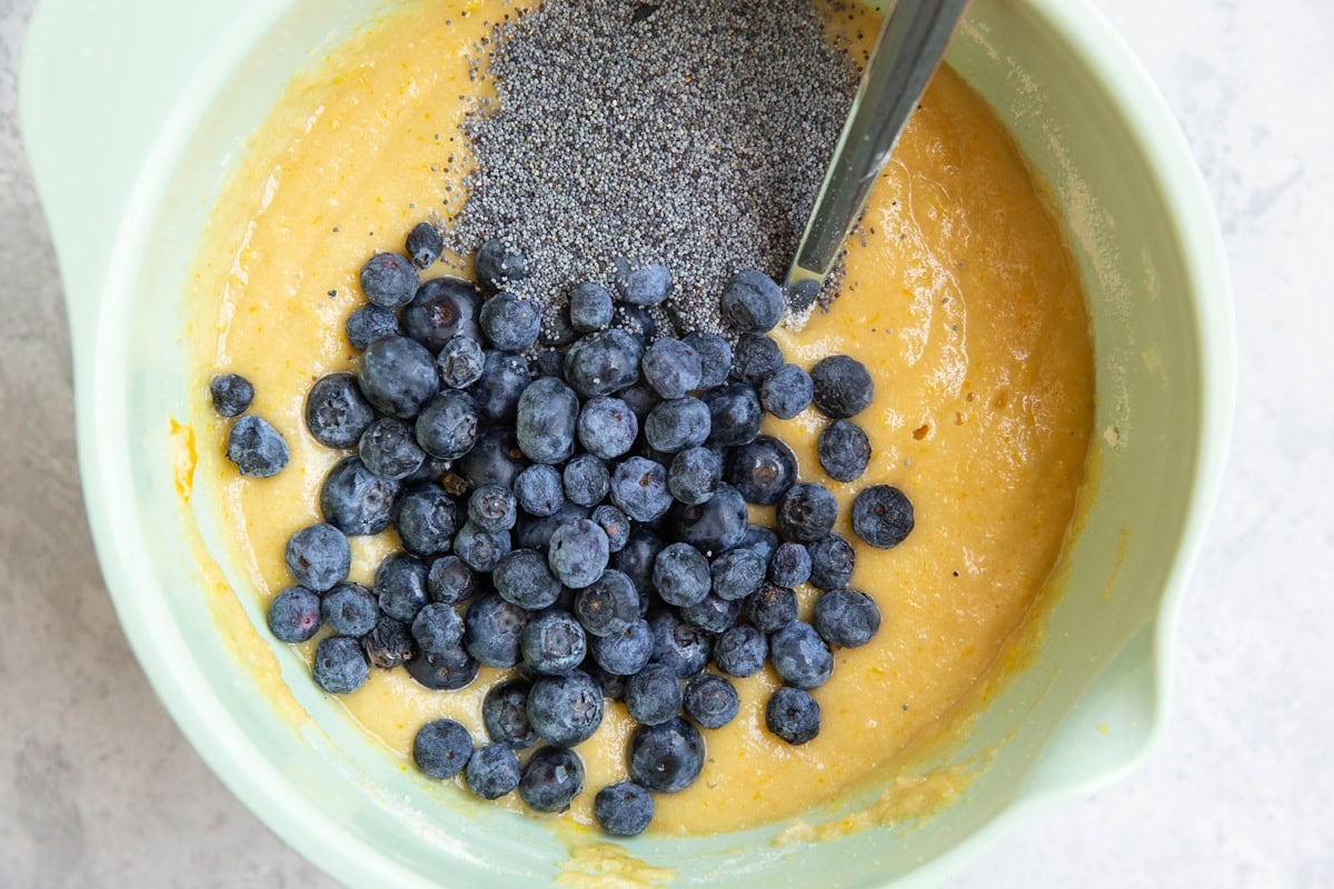 Lemon cake batter in a mixing bowl with blueberries and poppy seeds.