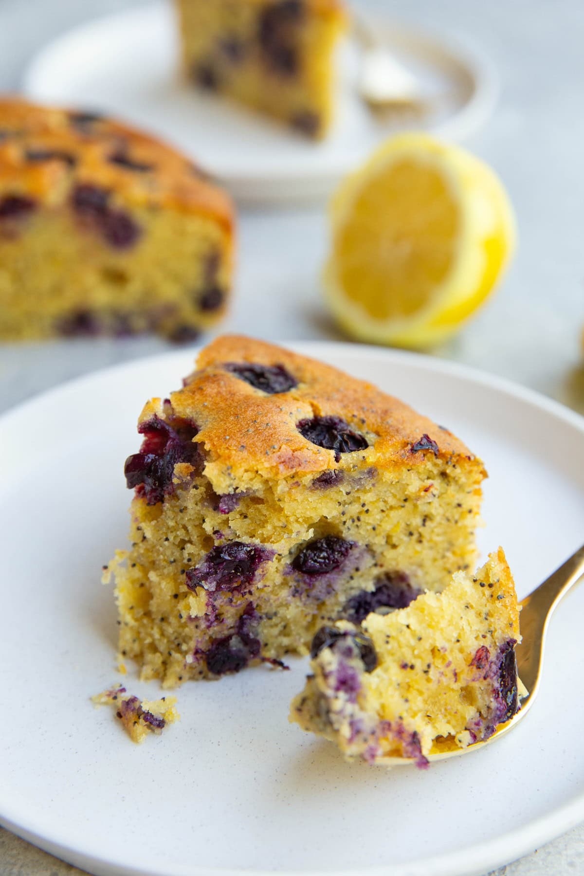 Slice of lemon poppy seed blueberry cake with a bite taken out.