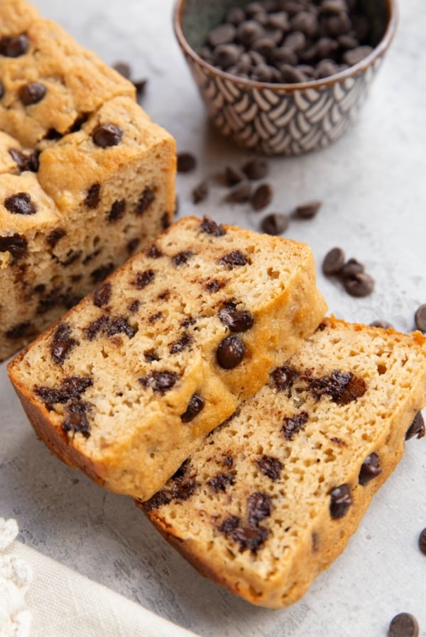 Loaf of chocolate chip bread on a background cut into slices with chocolate chips sprinkled around.