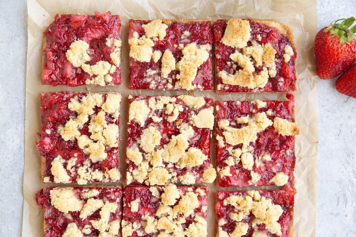 Strawberry crumb bars cut into slices on a sheet of parchment paper with fresh strawberries to the side.