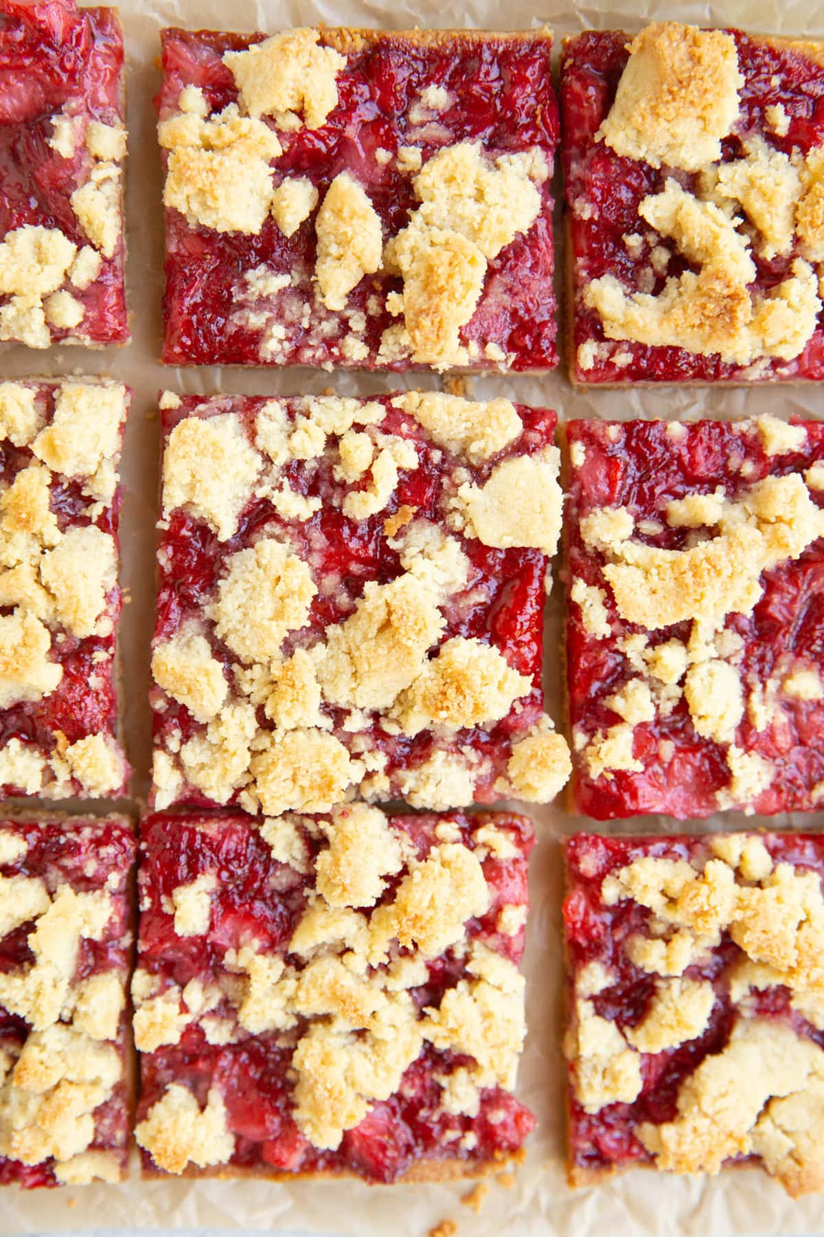 Strawberry crumb bars cut into slices on a sheet of parchment paper, ready to serve.