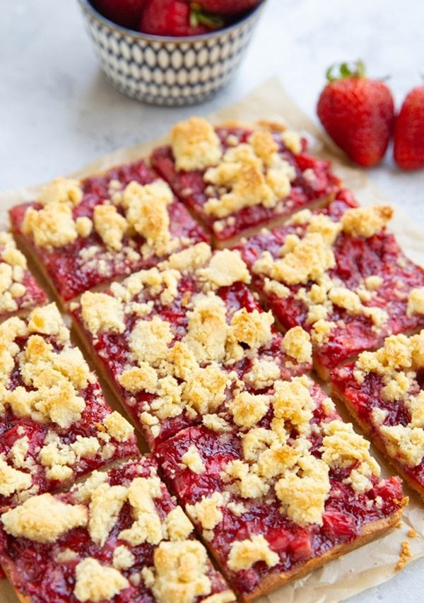 Strawberry crumb bars cut into slices on a flat surface with fresh strawberries in the background.
