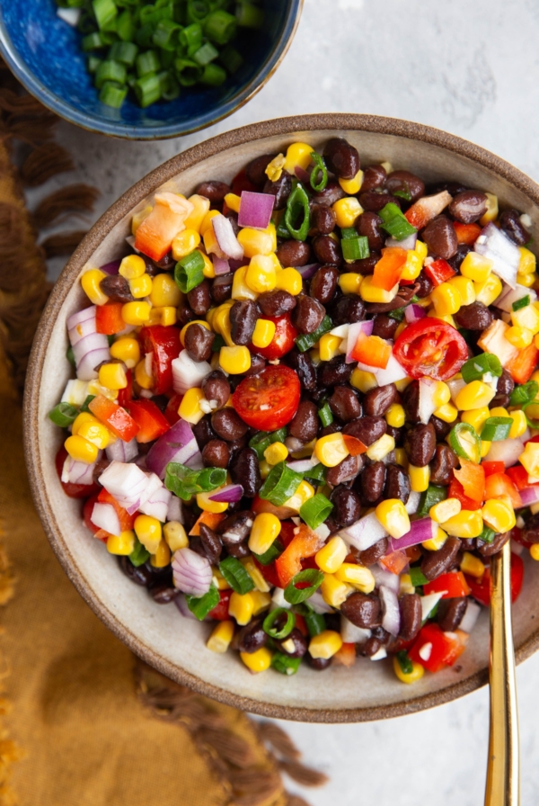 Bowl of black bean salad with onions, tomatoes, and corn.