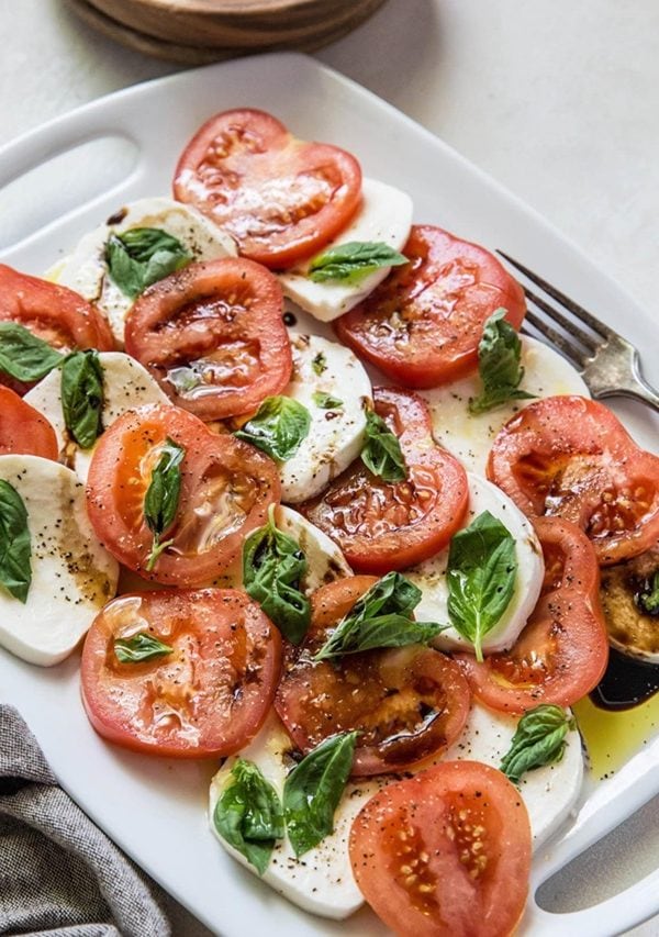 White platter of caprese salad with fresh basil