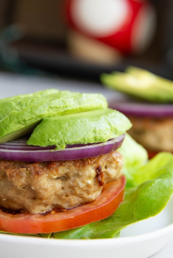 Chicken burger patty on top of lettuce and tomato with avocado and onion on top, ready to serve.
