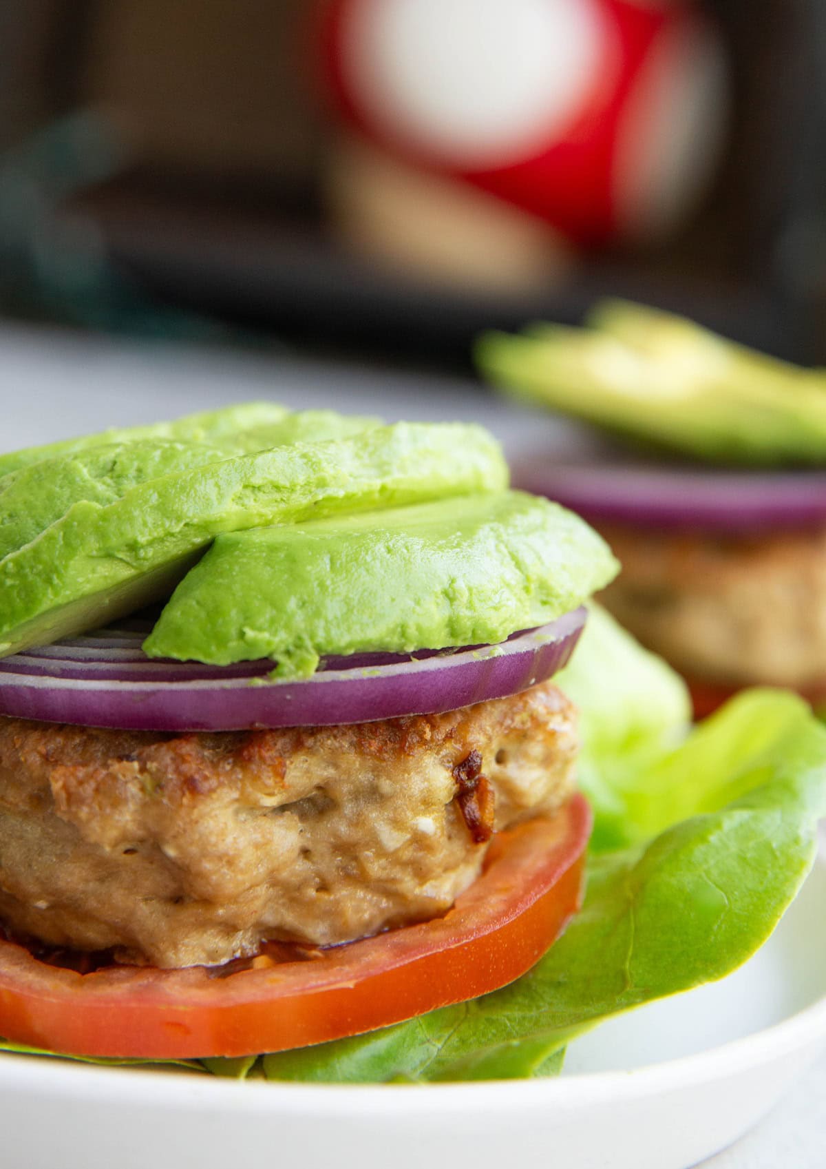 Chicken burger patty on top of lettuce and tomato with avocado and onion on top, ready to serve.