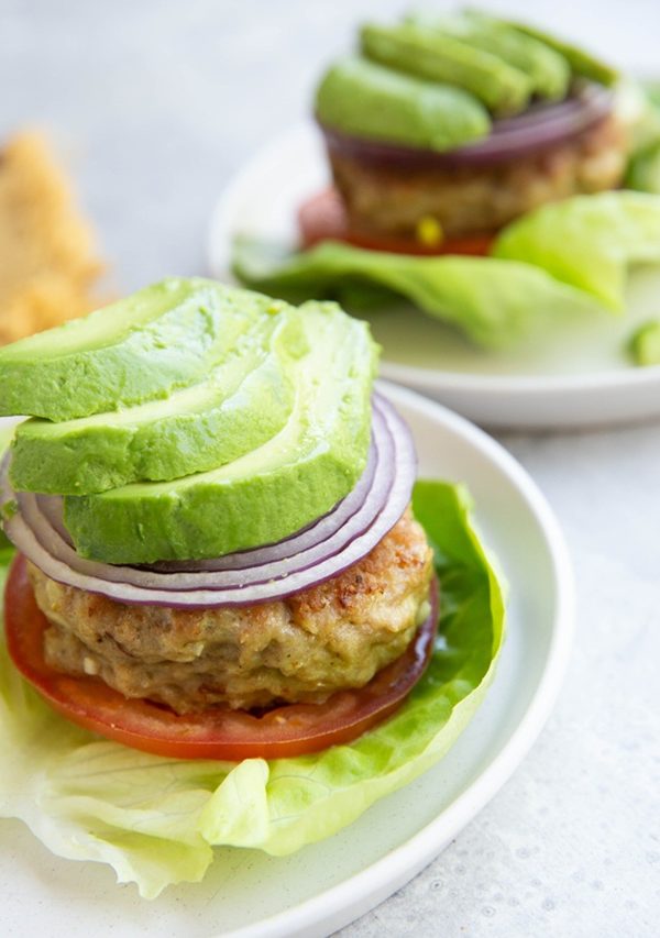 Chicken burger patties on lettuce with onion, tomatoes, and avocado