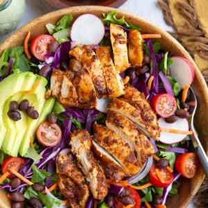 Large bowl of taco salad with fresh spring greens, black beans, sliced avocado, cherry tomatoes, cabbage, and more.