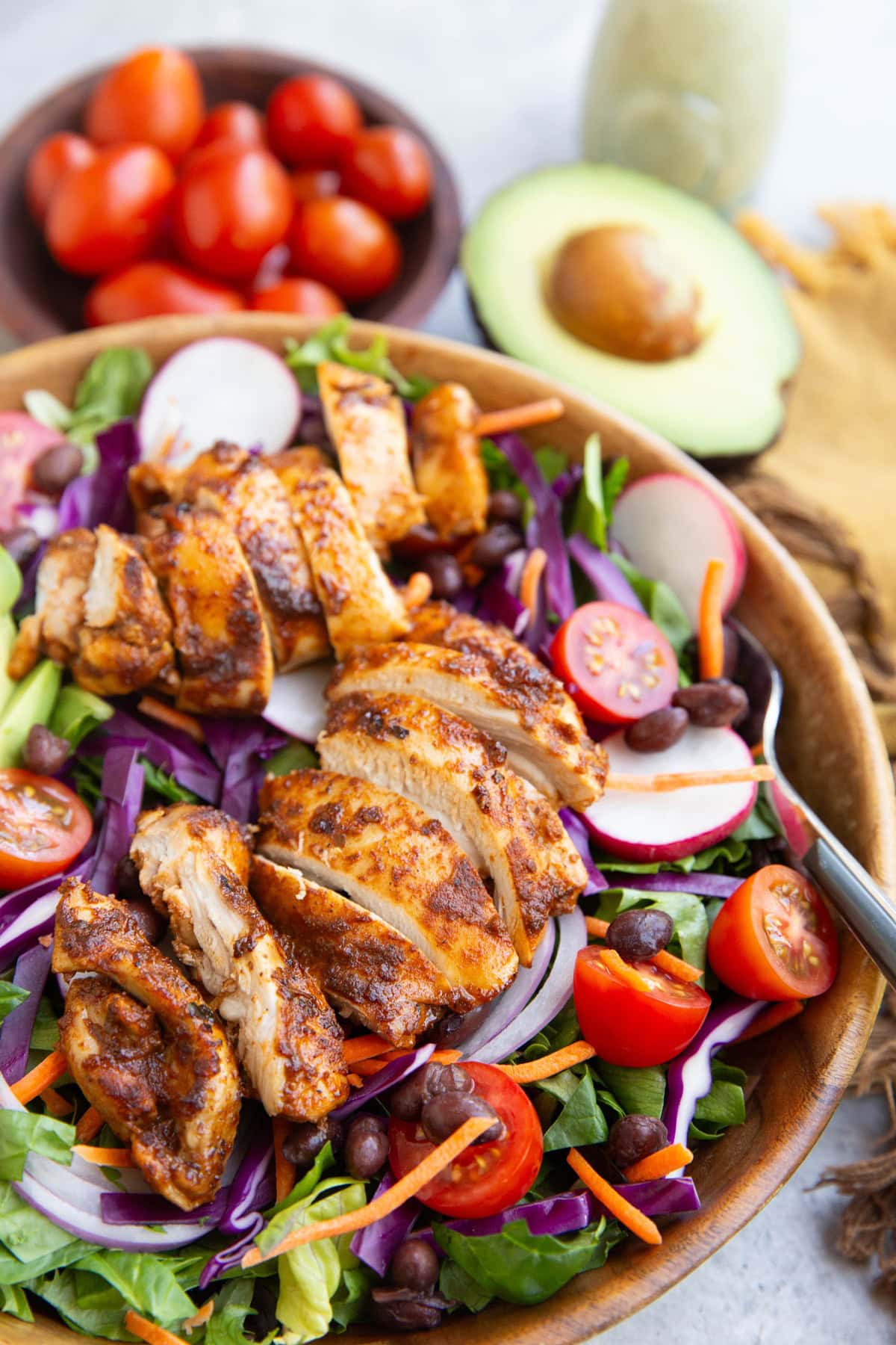 Large taco salad in a wooden bowl with chicken, spring greens, tomatoes, black beans, and more.