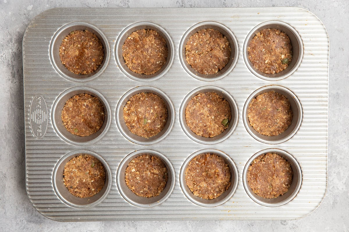 Muffin tray with energy bite mixture inside, pressed into even layers.
