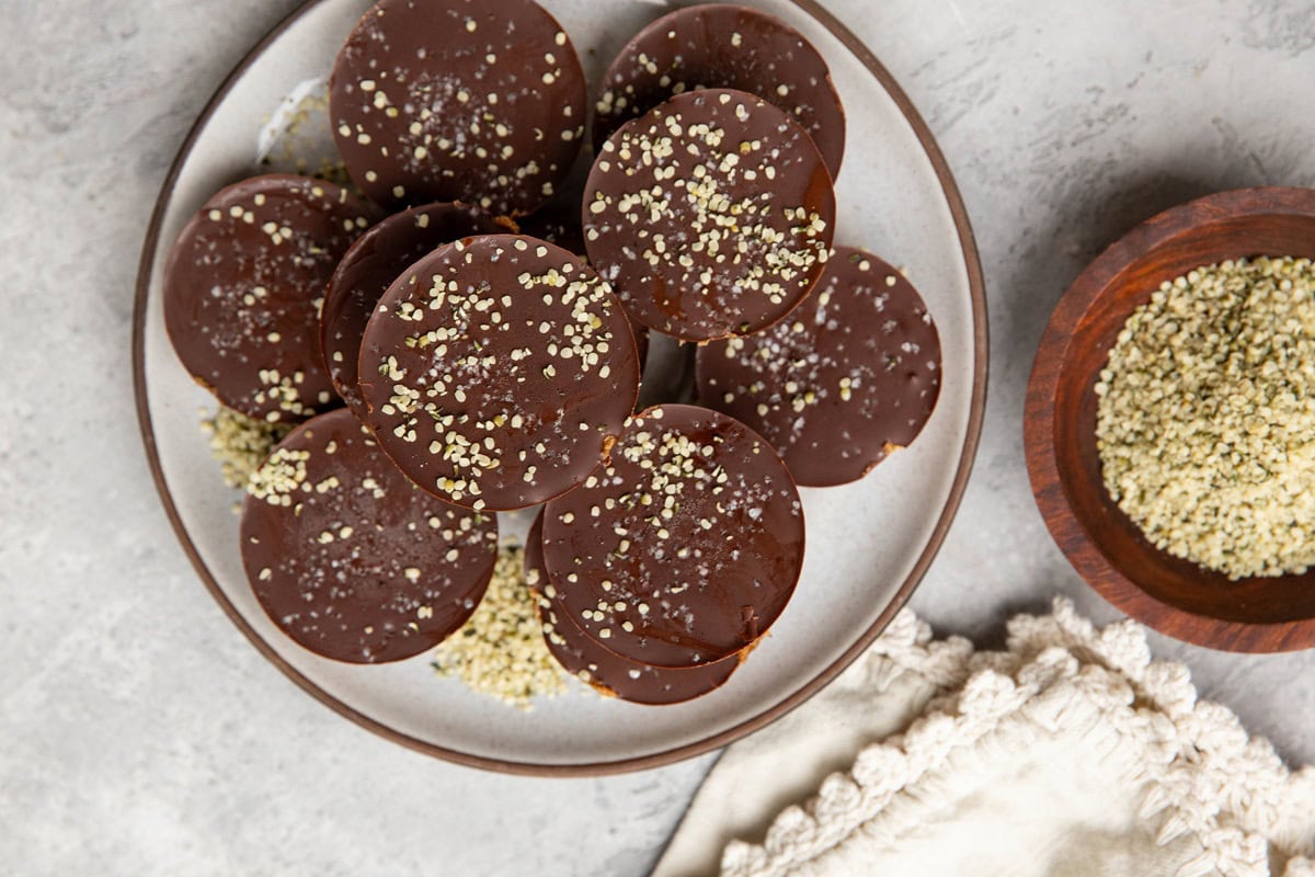 Chocolate covered energy cups sitting in a pile on a plate with a bowl of hemp seeds to the side.