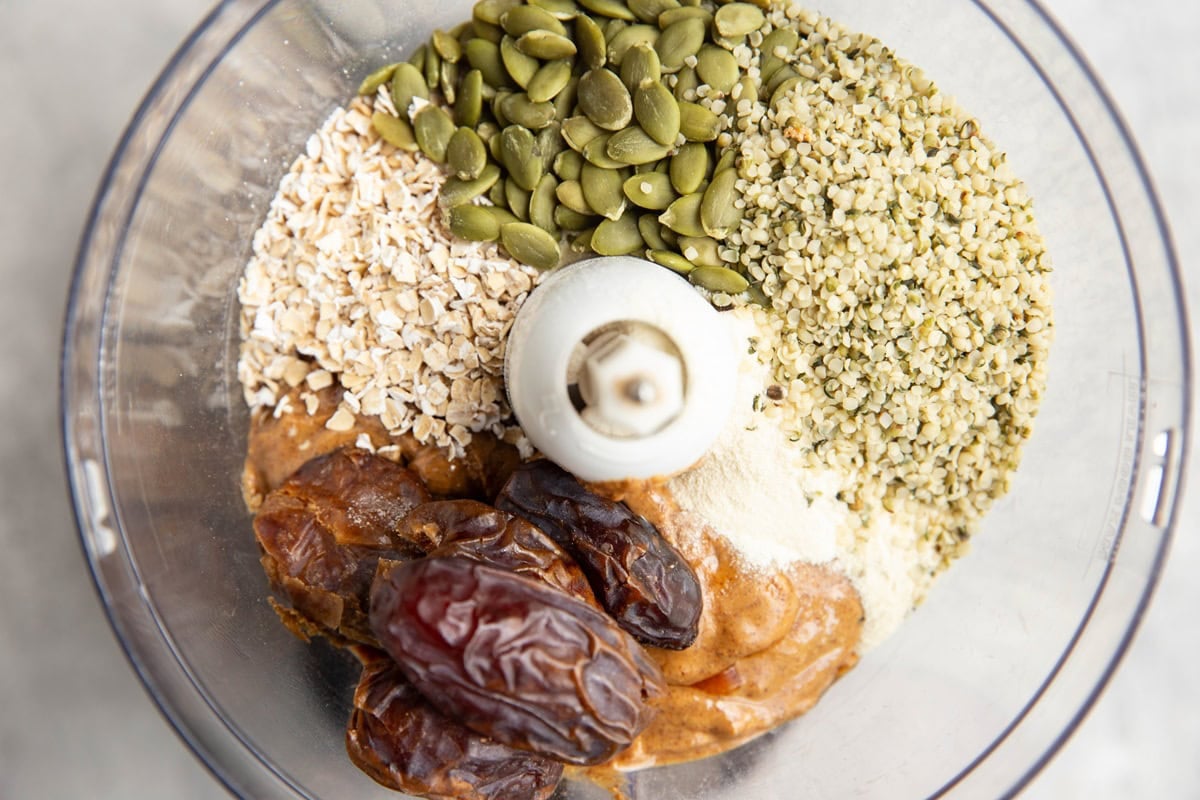 almond butter, hemp seeds, pumpkin seeds, oats, and protein powder in a food processor, waiting to be processed.