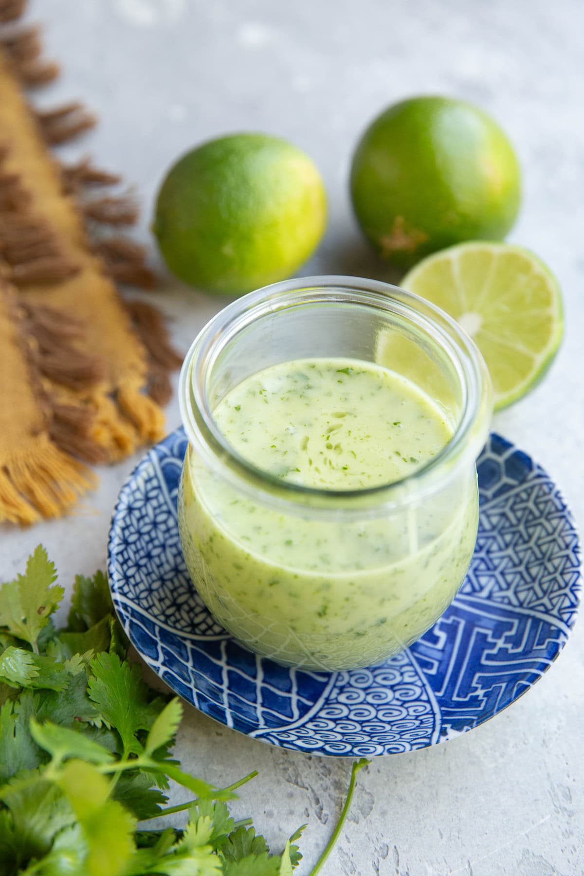 Small jar of cilantro dressing on a blue plate with fresh limes in the background. Ready to be used.