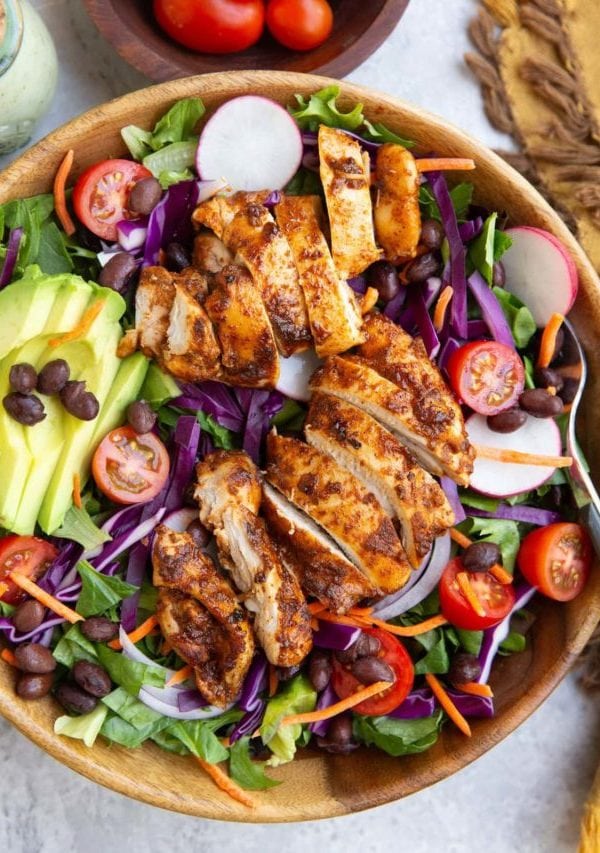 Large bowl of taco salad with fresh spring greens, black beans, sliced avocado, cherry tomatoes, cabbage, and more.