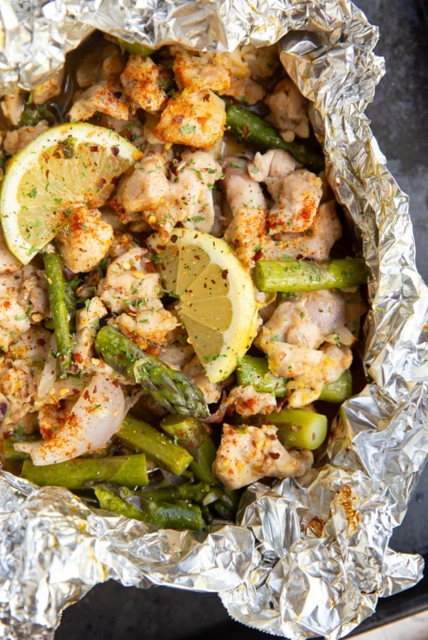 Chicken, asparagus, and lemons cooked in a foil packet. Foil packet is open to reveal the finished result.