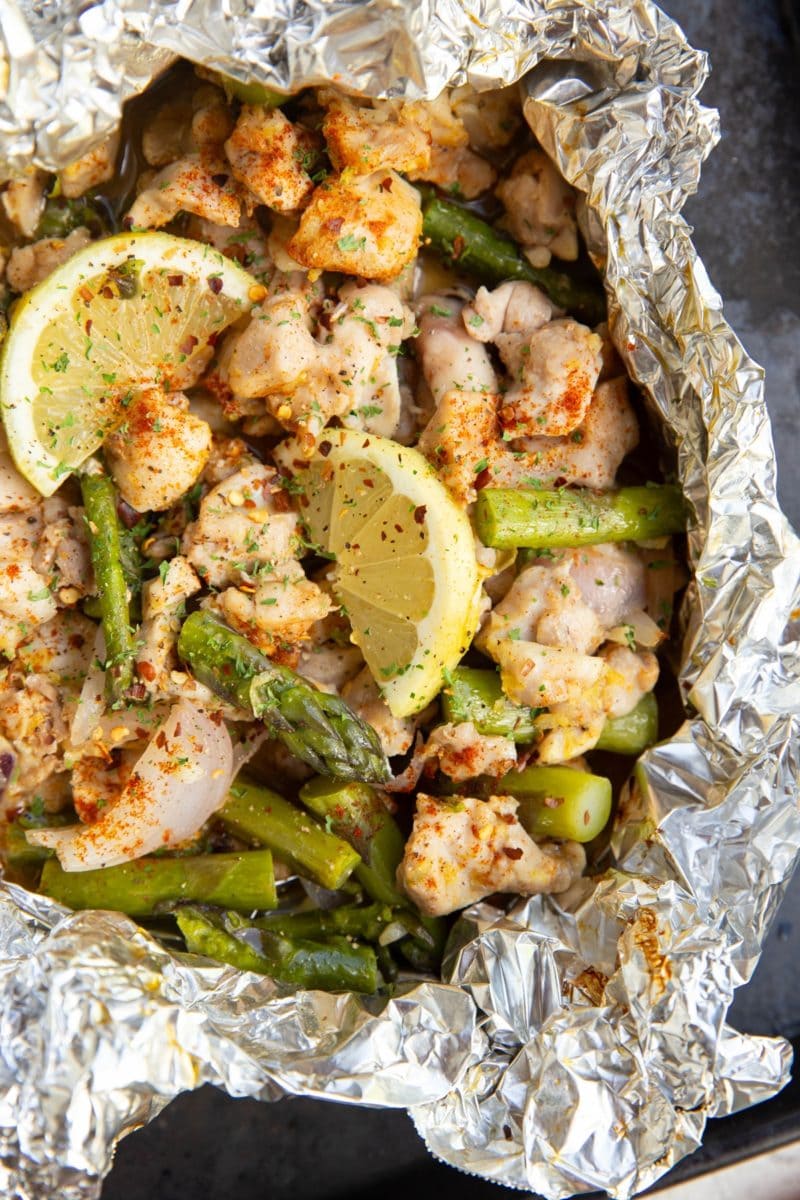 Chicken, asparagus, and lemons cooked in a foil packet. Foil packet is open to reveal the finished result.