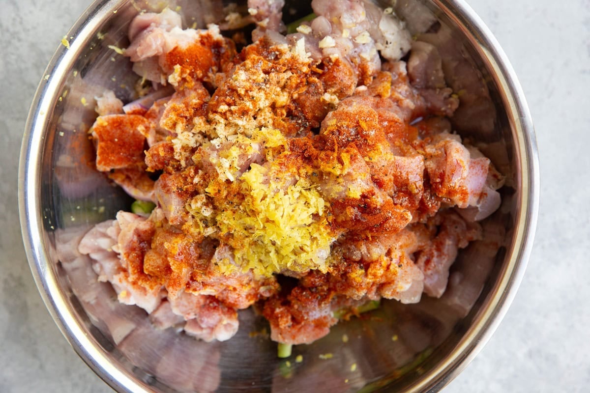 Stainless steel mixing bowl full of chopped chicken, asparagus, seasonings, garlic, and lemon zest.