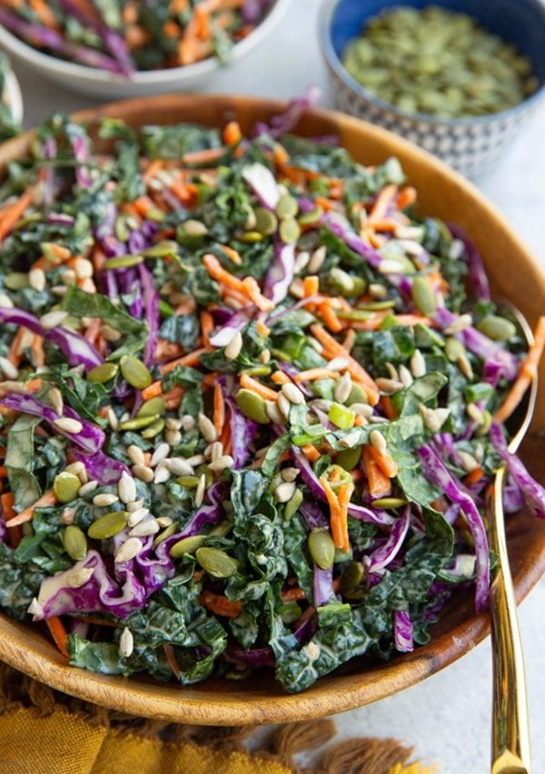 Kale slaw in a wooden bowl with a gold spoon, ready to serve.