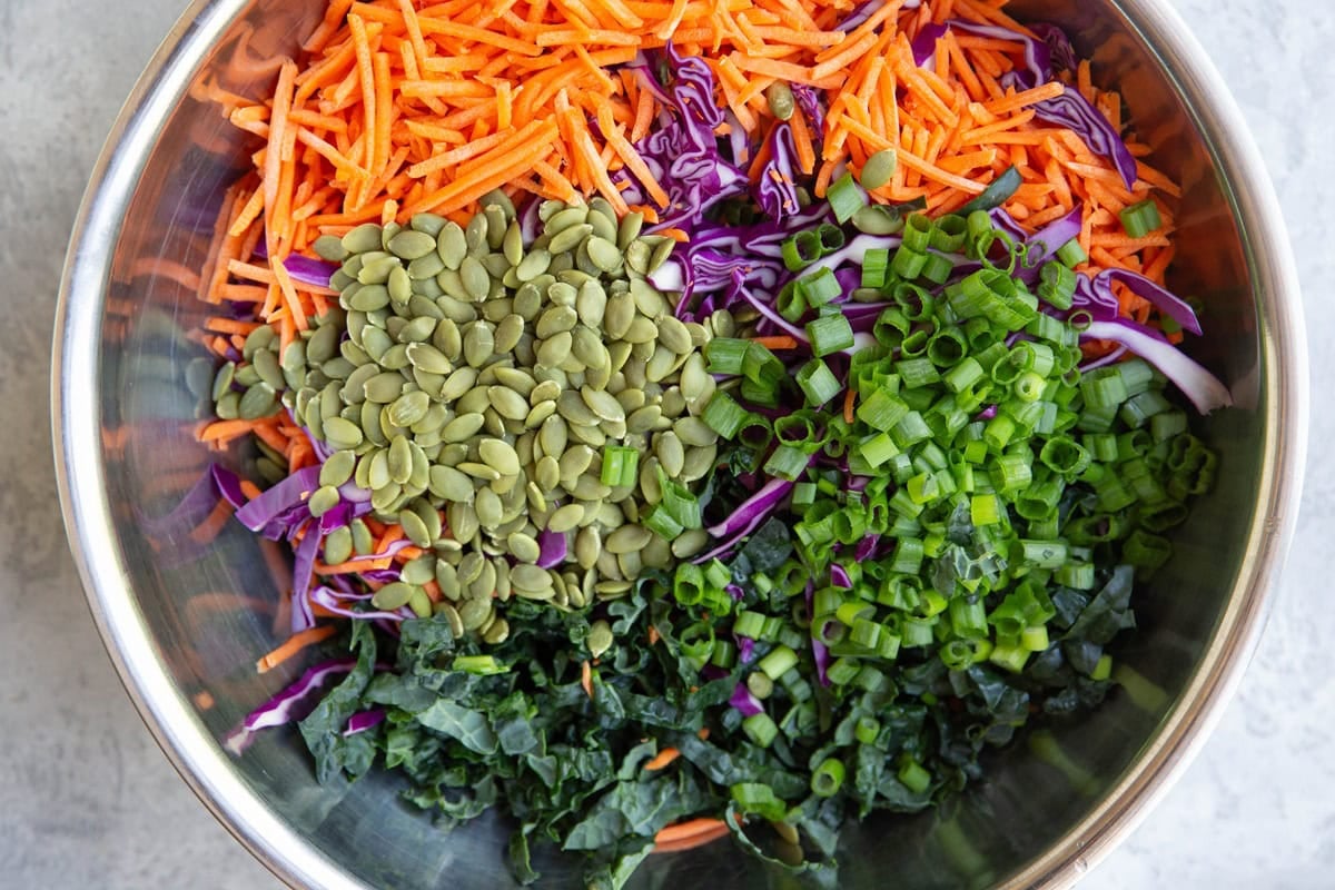 Stainless steel bowl full of kale, carrots, cabbage, green onions, and pumpkin seeds.