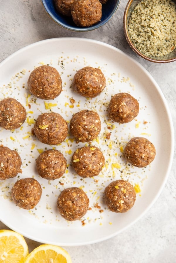 Lemon Poppy Seed Energy Balls on a plate with a bowl of hemp seeds to the side and a fresh lemon cut in half.