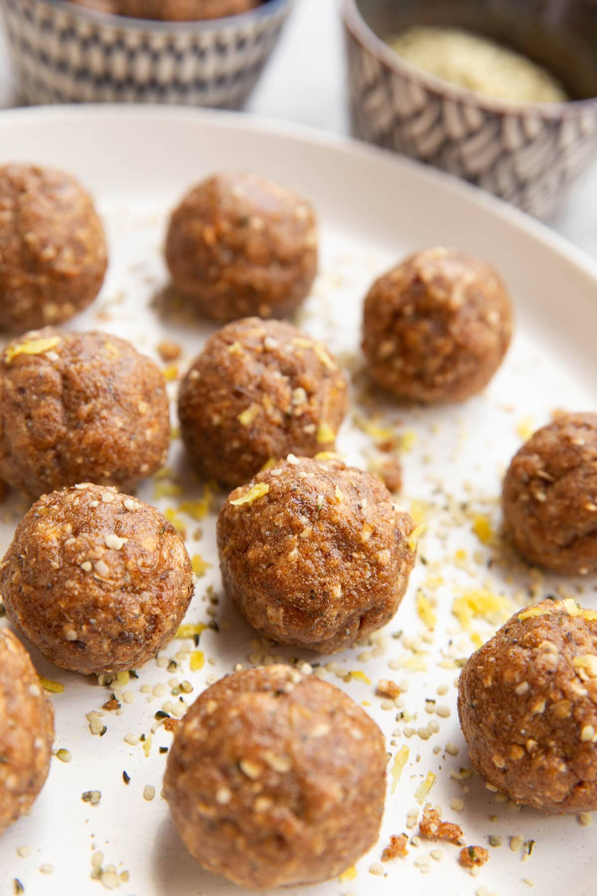 Lemon poppy seed energy balls on a plate, sprinkled with lemon zest and hemp seeds.