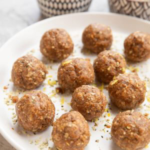 Plate of energy balls sprinkled with lemon zest. Two bowls of balls and seeds in the background.