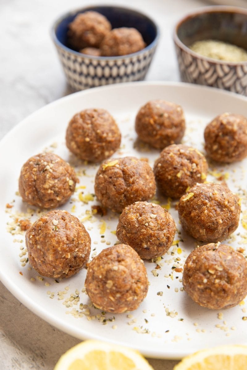 Plate of energy balls sprinkled with lemon zest. Two bowls of balls and seeds in the background.