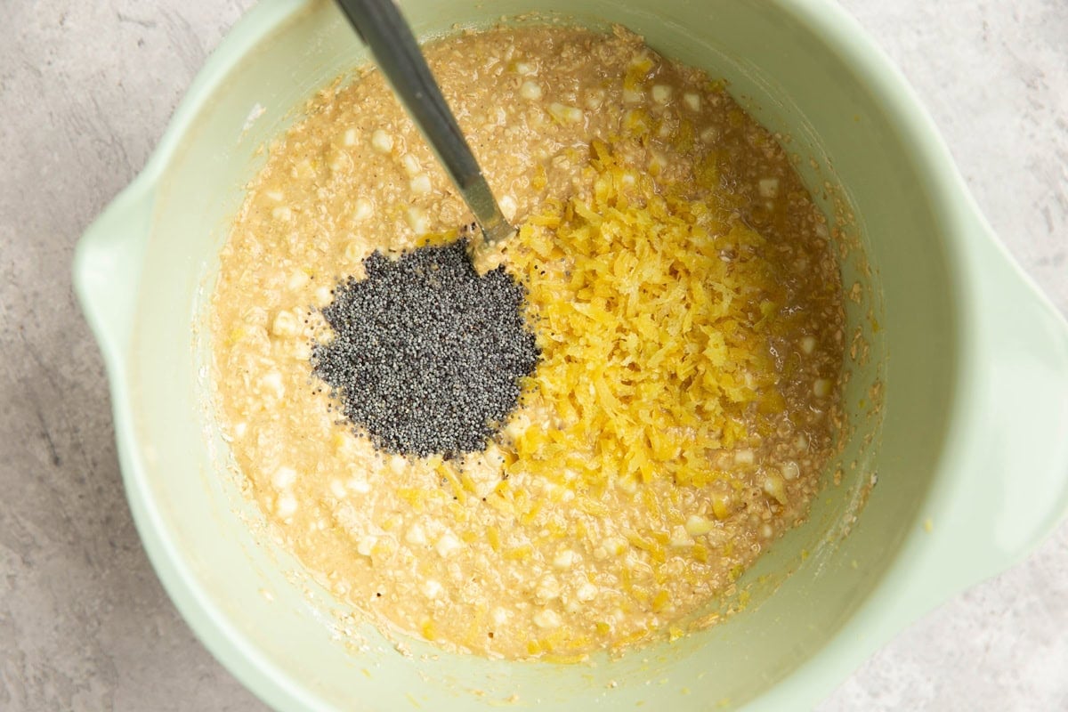 Lemon poppy seed bread batter in a mixing bowl with lemon zest and poppy seeds on top, ready to be mixed in.