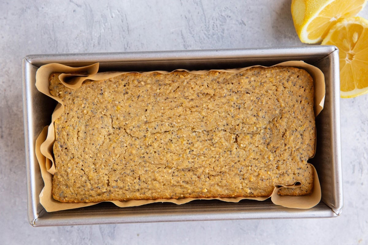 Lemon poppy seed bread in a loaf pan with fresh lemons to the side, fresh out of the oven.