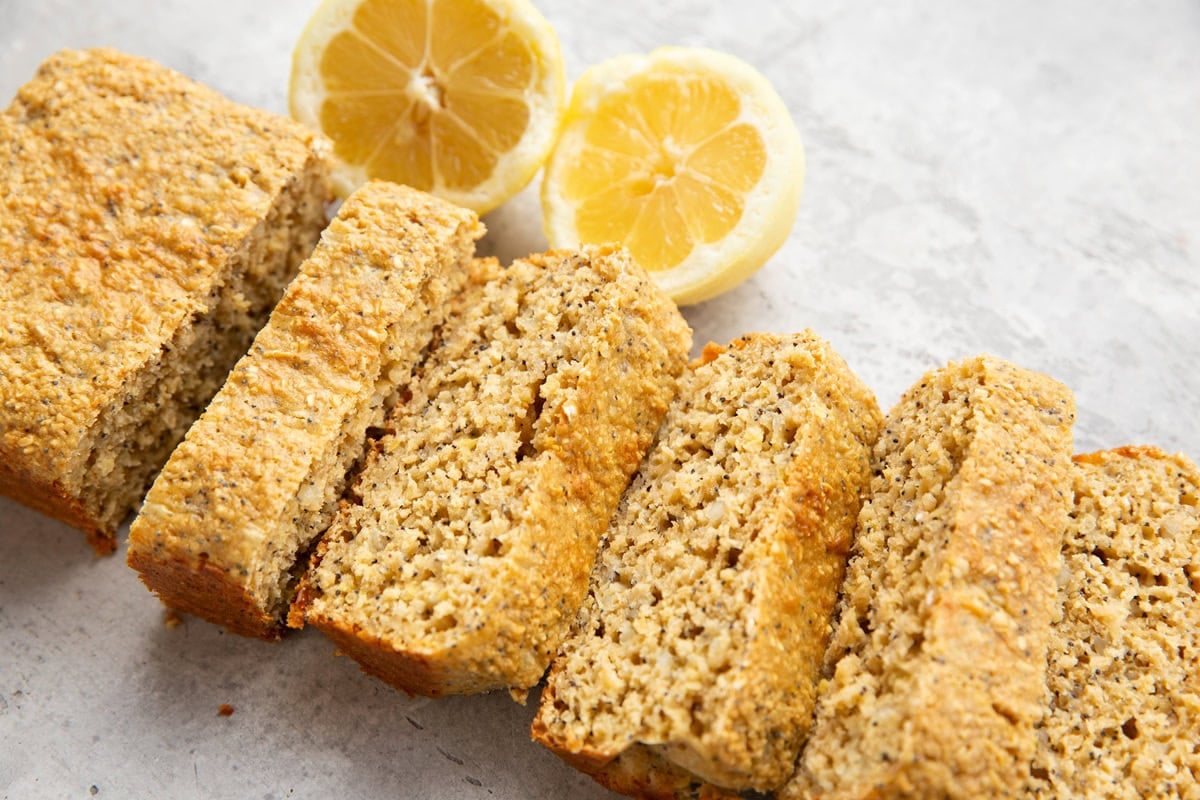 Loaf of lemon poppy seed bread cut into thick slices with lemons in the background