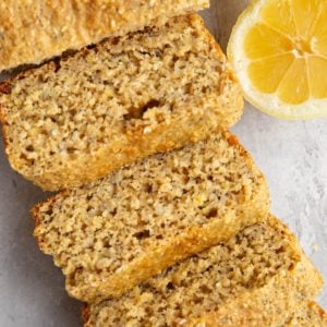 Lemon poppy seed loaf cut into slices with fresh lemons to the side.