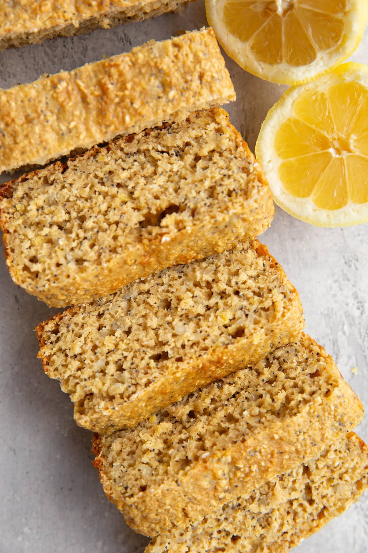 Lemon poppy seed loaf cut into slices with fresh lemons to the side.