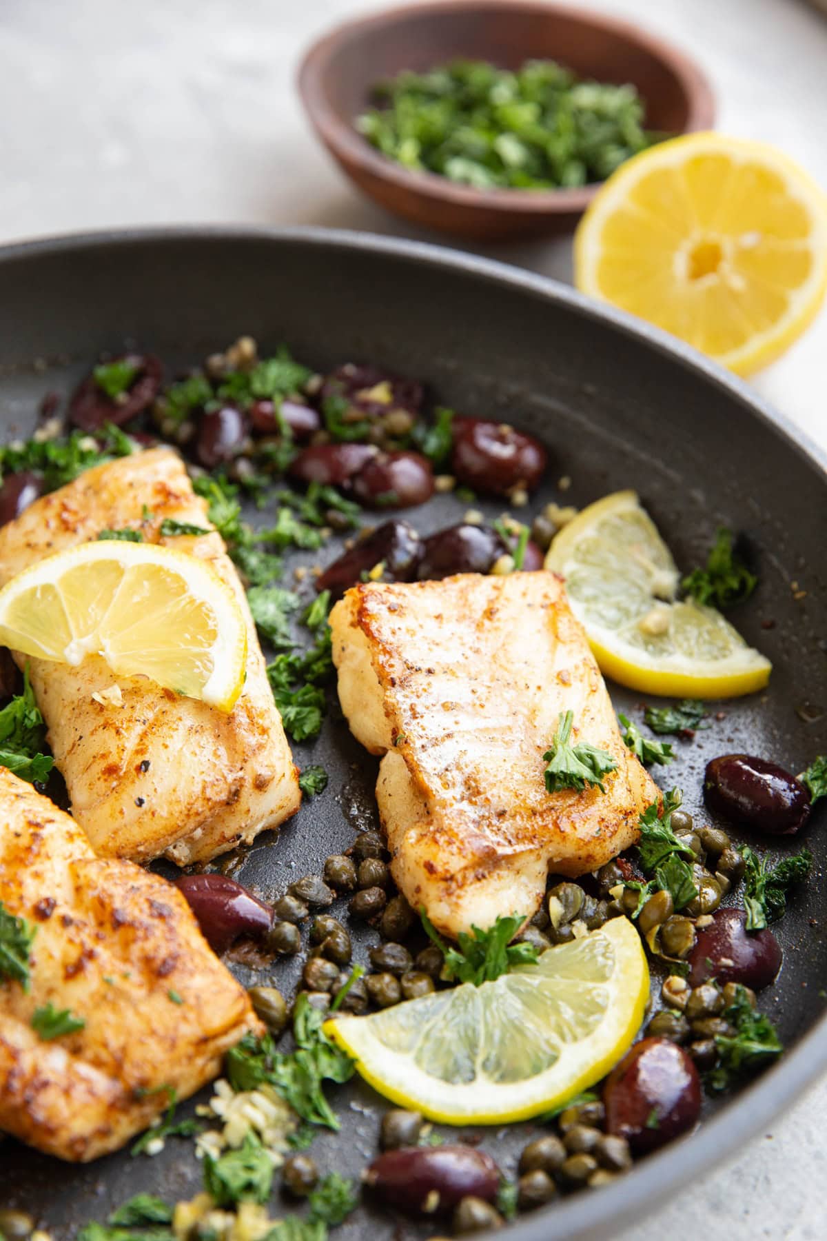 Skillet of seared cod with olives, capers, and lemon.