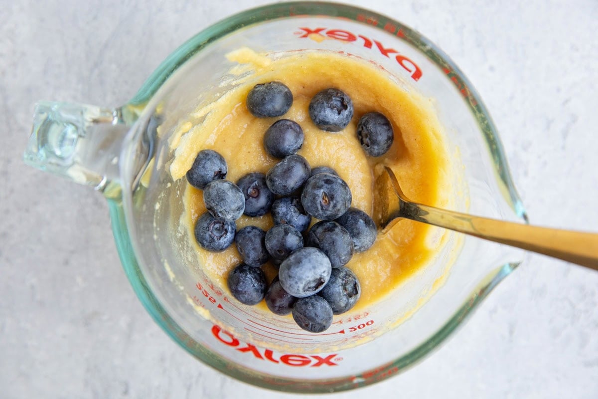 Measuring cup full of single-serve muffin batter with blueberries on top, ready to be mixed in.