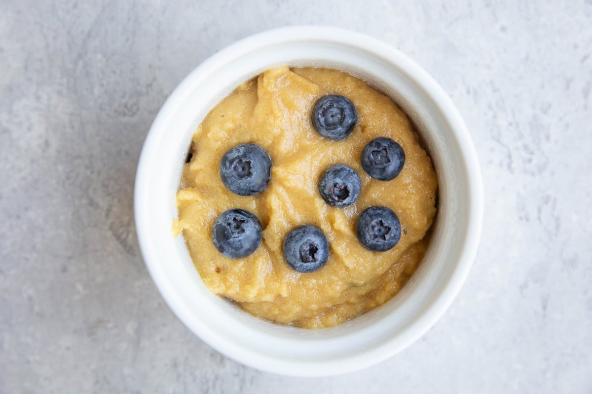 Ramkekin with batter for a single muffin inside and blueberries on top, ready to bake.