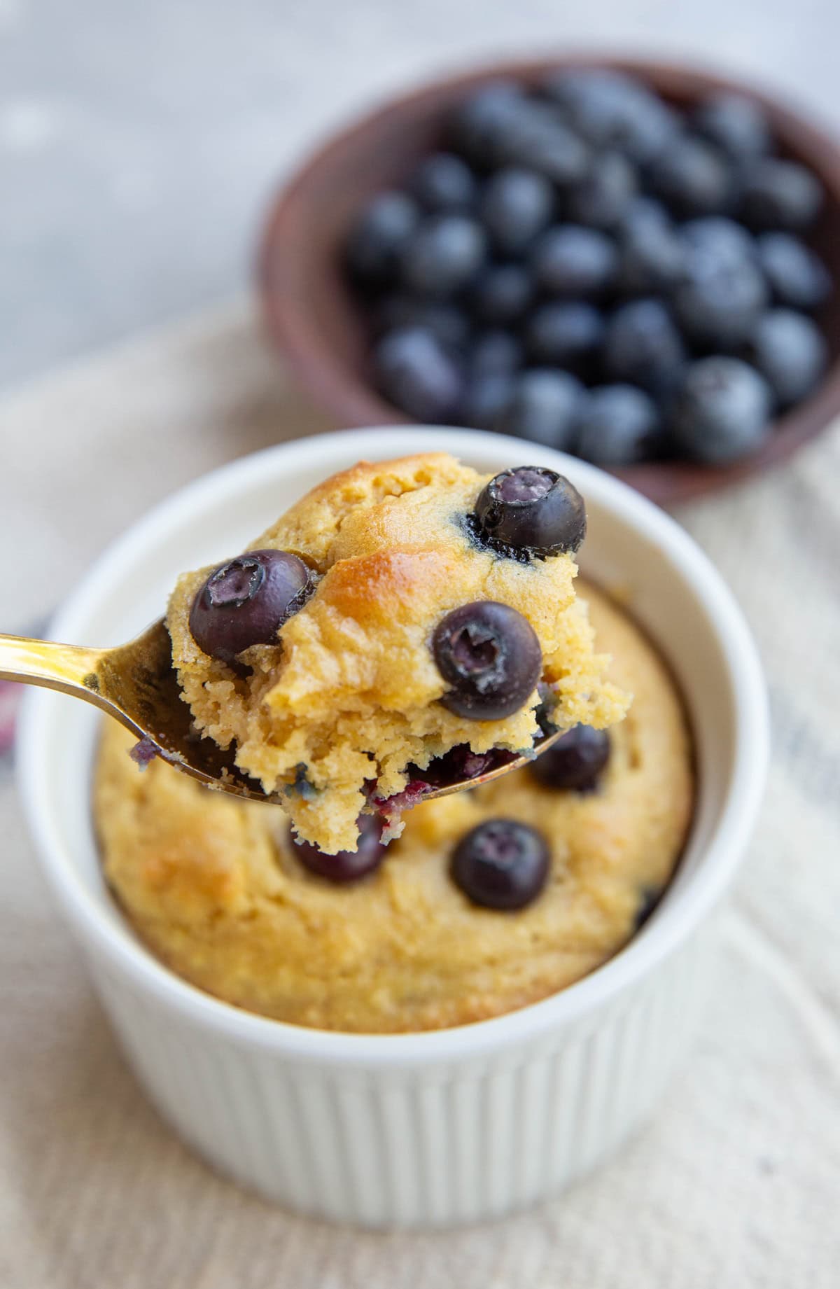 Blueberry muffin in a ramekin with a bite being taken out.