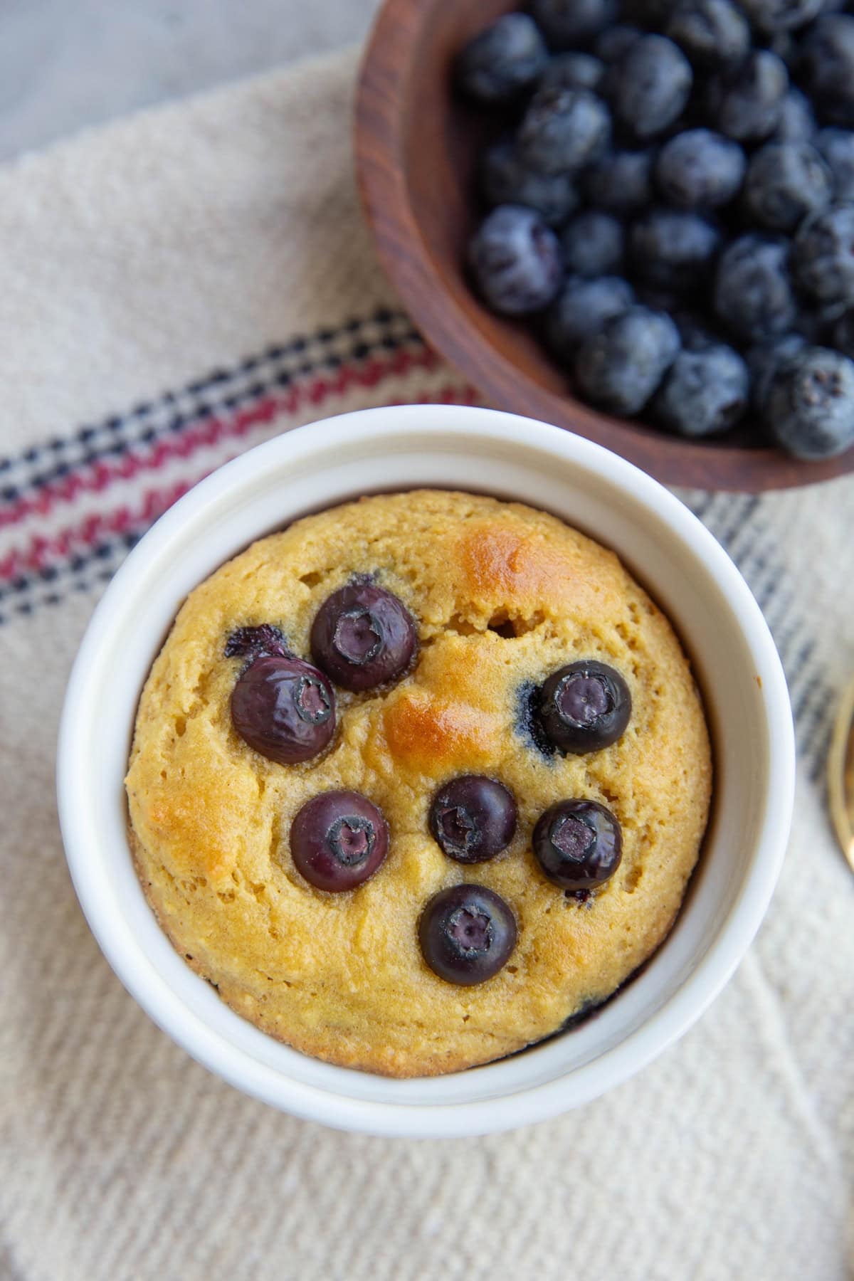 Ramekin with one blueberry muffin inside and a bowl of fresh berries to the side.