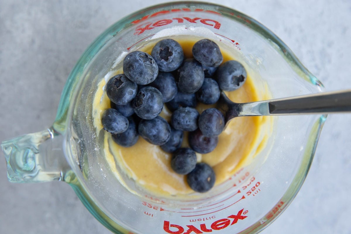 Fresh blueberries on top of muffin batter in a measuring cup, ready to be mixed in.